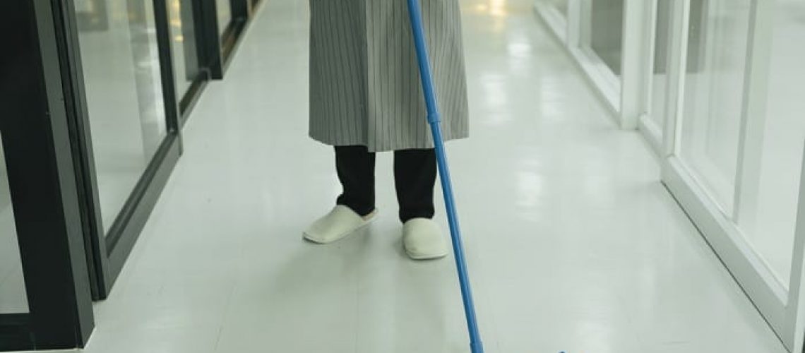 Maid using mop cleaning the floor in condo apartment room.